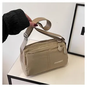 Détails de la bandoulière en nylon kaki avec plusieurs compartiments zippés et logo blanc