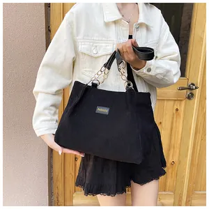Detail of black corduroy tote bag featuring fashion label and metal chain handle strap