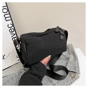 Détail d'un sac bandoulière en nylon noir avec texte gaufré et sangle réglable