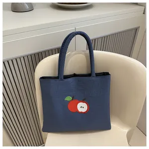 Close-up of apple embroidery on navy blue canvas tote bag placed on a wooden chair