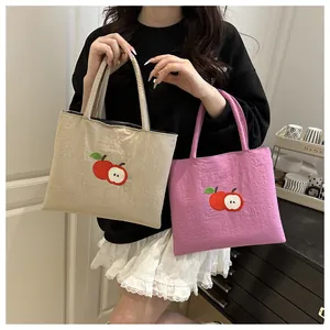Detailed view of tote bags featuring embroidered red apple design on nylon fabric
