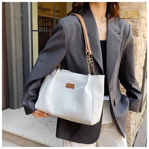 Close-up of white corduroy tote bag with brown leather label and metal chain strap