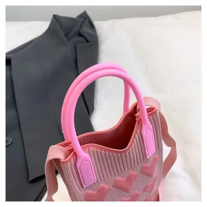 Close-up of pink knitted bag with heart patterns, showing round handles and shoulder strap