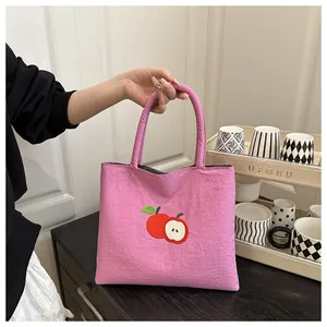 Close-up of pink canvas tote bag featuring a red apple embroidery and dual handles