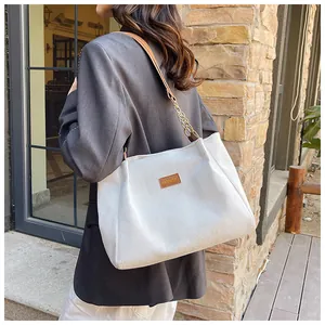 Detail of white corduroy tote bag featuring leather strap and gold chain accent