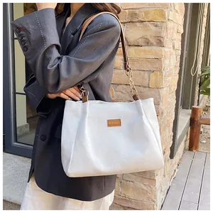 Detail of white corduroy tote bag with brown leather label and golden chain strap
