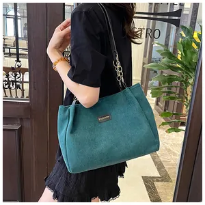 Detail of dark green corduroy tote bag with fashion label and metal chain strap