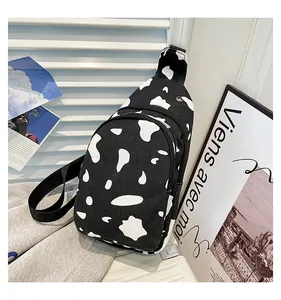 Detail of cow print canvas chest bag featuring dual zippers and black woven strap