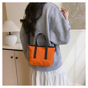Gros plan sur un petit sac fourre-tout orange avec bandoulière et poignées noires
