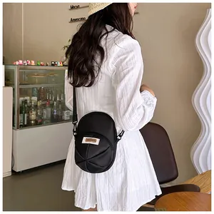 Modern black nylon crossbody bag with pleated base shown on model in cafe setting