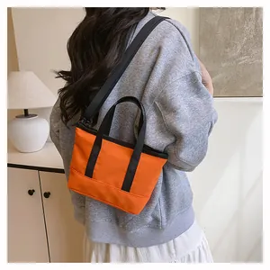Vue latérale d'un mini sac à bandoulière orange vif avec poignées noires sur modèle
