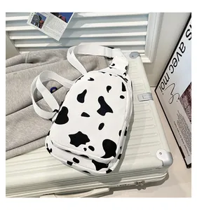 Detail shot of canvas cow print chest bag showing zipper compartments on a silver suitcase