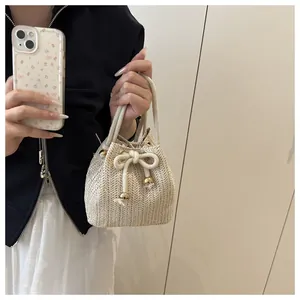 Detail of off-white straw bucket bag featuring drawstring closure and golden beads