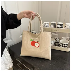 Close-up of beige canvas handbag featuring red apple embroidery with soft fabric texture