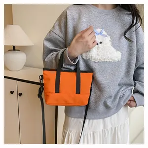 Gros plan du mini sac à bandoulière orange vif en toile avec poignées et sangle noires