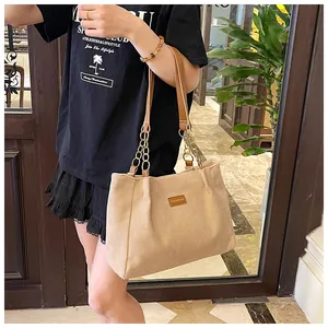 Detail of beige corduroy tote bag with brown leather handles and golden chain accents