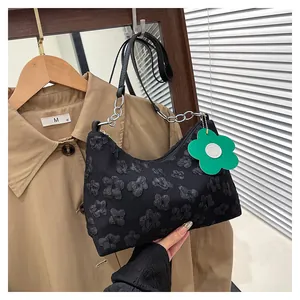 Detail of black floral shoulder bag with 3D flower texture and green pendant charm
