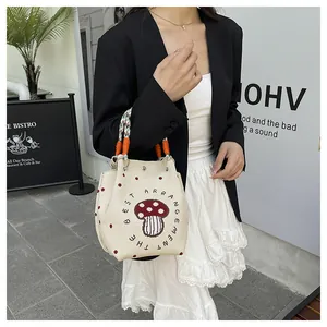 Detail of knit bucket bag with red mushroom embroidery and woven rope handle