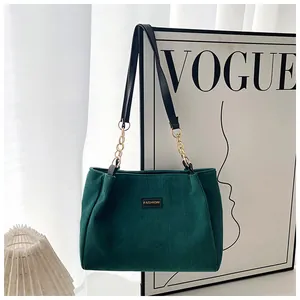 Close-up of green corduroy tote bag with black leather strap and metal chain details