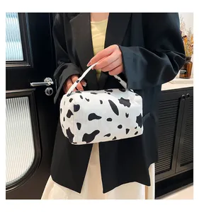 Detail of cow print corduroy makeup bag held by a model with black and white texture