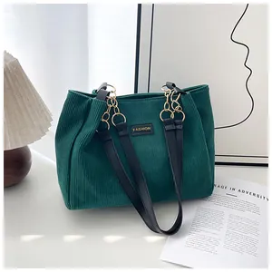 Detailed close-up of dark green corduroy tote bag with black straps and golden chain decoration