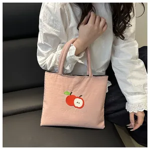 Pink canvas tote bag featuring detailed red apple embroidery held by a model