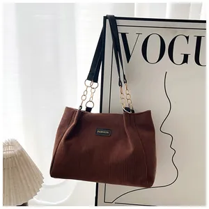 Close-up of brown corduroy tote bag with black fashion label and gold chain strap