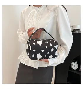Detail view of a cow pattern corduroy pouch held by a model in a cozy indoor setting