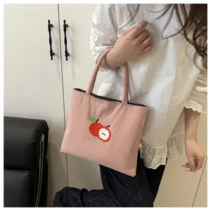 Detailed view of pink canvas tote bag with embroidered apple pattern held by model