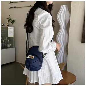 Model wearing dark blue round nylon crossbody bag with unique pleated stitching detail