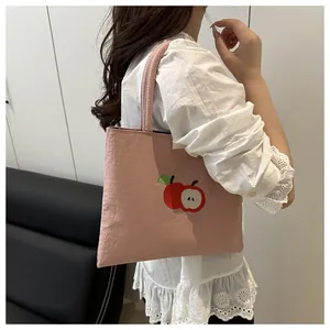 Close-up of pink canvas tote bag with red apple embroidery on a female shoulder