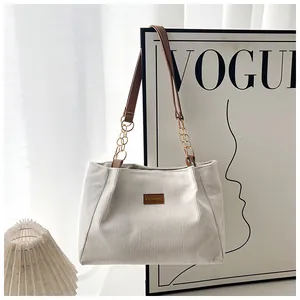 Detail of corduroy tote bag featuring a leather logo tag and chain strap for style