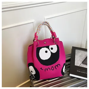 Detail of fuchsia knit tote bag with black eyes and mom text on a suitcase