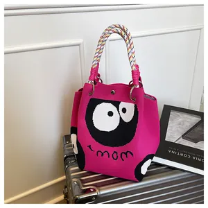 Detail of knit tote bag featuring large eye cartoon and colorful braided rope handle