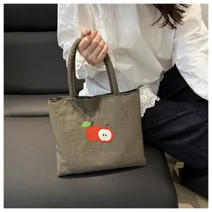 Detail of khaki green canvas tote bag featuring delicate red apple embroidery and soft handles