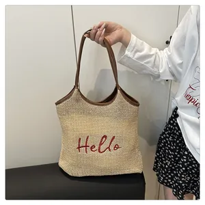 Detailed close-up of woven straw tote bag featuring red Hello embroidery and leather handles