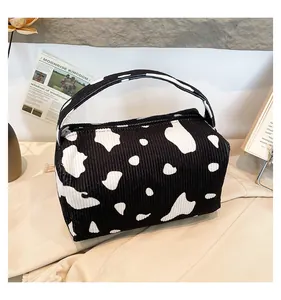 Detail of a cow print corduroy makeup bag showing fabric texture and portable handle