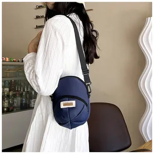 Detail shot of a dark blue nylon crossbody bag with a zipped pocket on a model