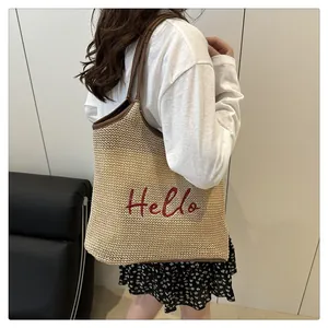 Detail of woven straw tote bag featuring red Hello embroidery and brown leather handles