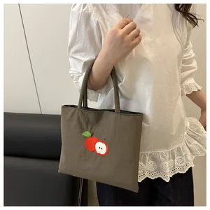 Detailed embroidery of red apples on olive brown canvas tote bag for daily casual use