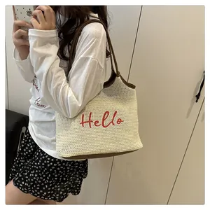 Close-up of woven straw tote bag with red Hello embroidery and brown leather trim detailing