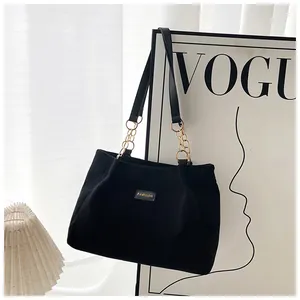 Detail of corduroy tote bag featuring a black leather strap and gold chain link