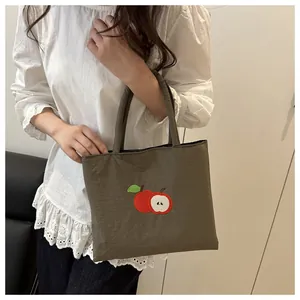 Detail of red apple embroidery on olive green canvas tote bag with textured fabric