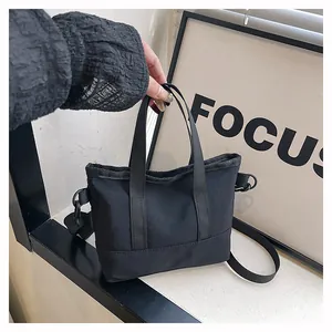 Détail du mini sac cabas en toile noire avec poignées tissées et bandoulière réglable