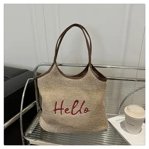 Close-up of beige woven straw tote bag featuring red Hello embroidery and brown leather handles