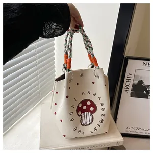 Close-up of knit tote bag with mushroom pattern and colorful braided rope handle