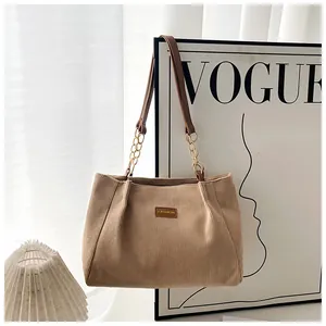 Detail of corduroy tote bag featuring leather label and gold chain shoulder strap