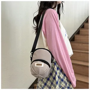 Detail of beige nylon cap-shaped crossbody bag with adjustable strap on a female model