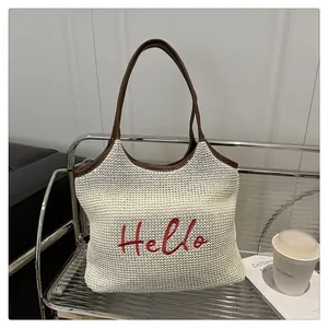Close-up of woven straw tote bag featuring red Hello embroidery and brown leather trim