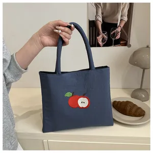 Detail of navy blue canvas tote bag with embroidered apple pattern on a vintage cabinet